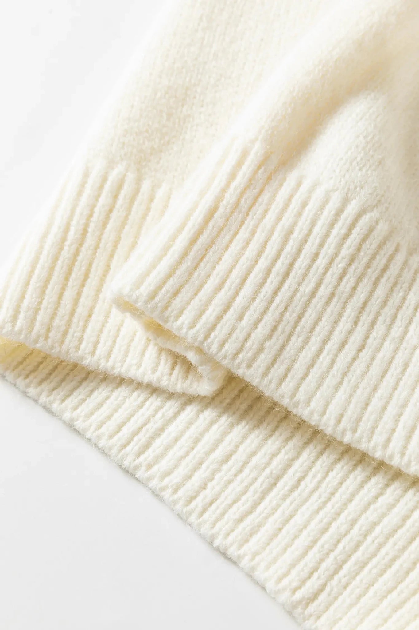 Close-up of a cream-colored ribbed knit fabric, showing the soft texture and folded layers of the material.
