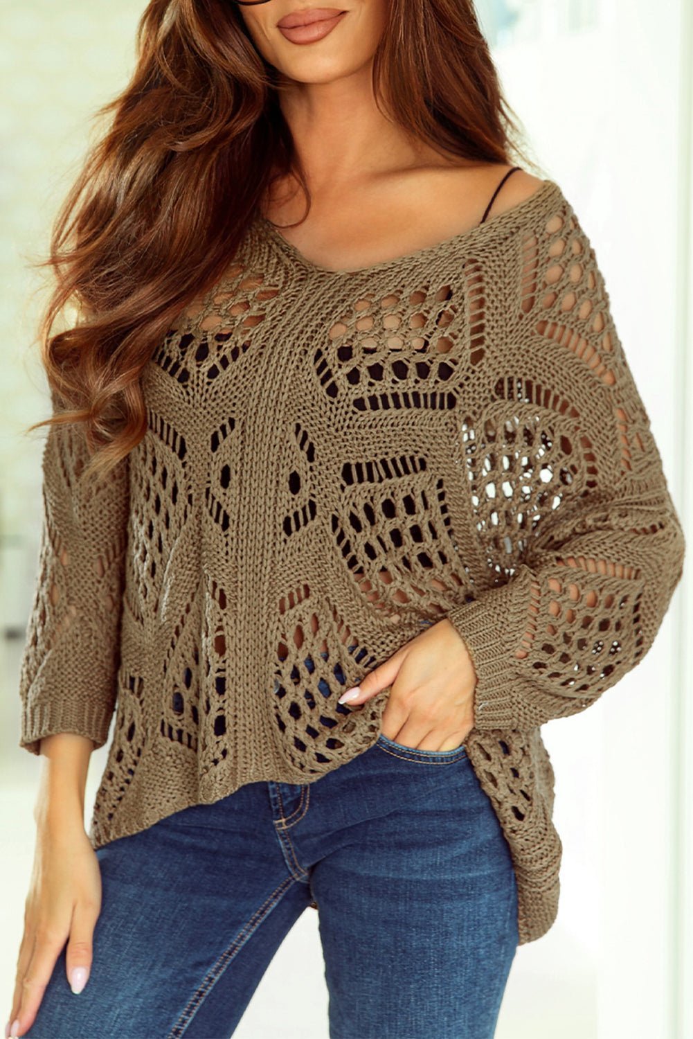 Woman wearing a brown crochet sweater and blue jeans against a light background