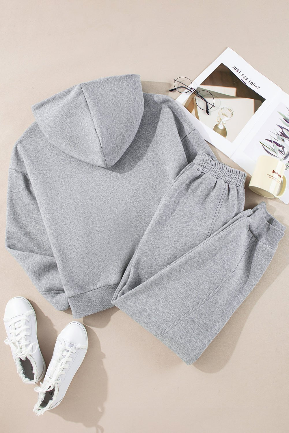 Gray hoodie and pants set with white sneakers on a beige surface