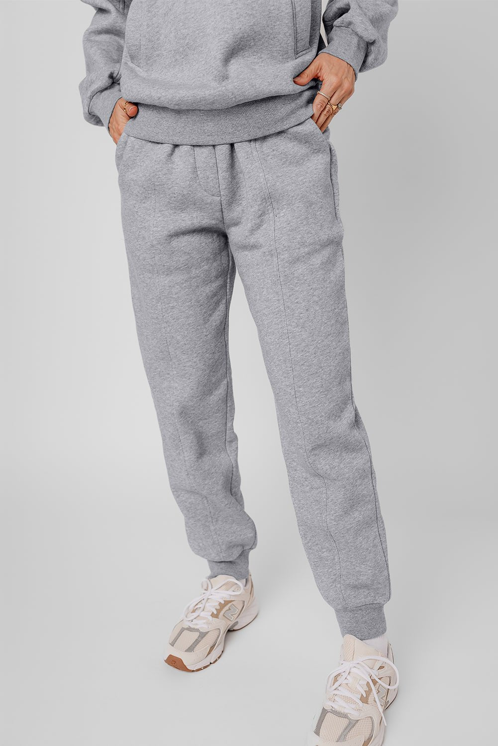 Person wearing a gray tracksuit with white sneakers on a light gray background