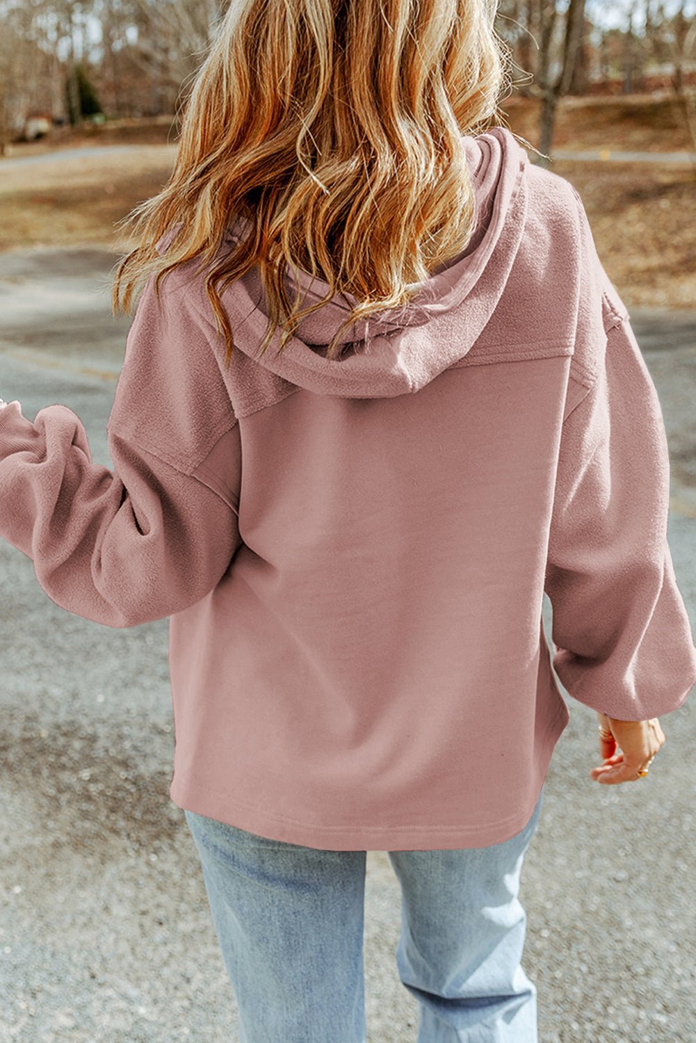 Person in pink hooded jacket outdoors on road with trees and grass background.