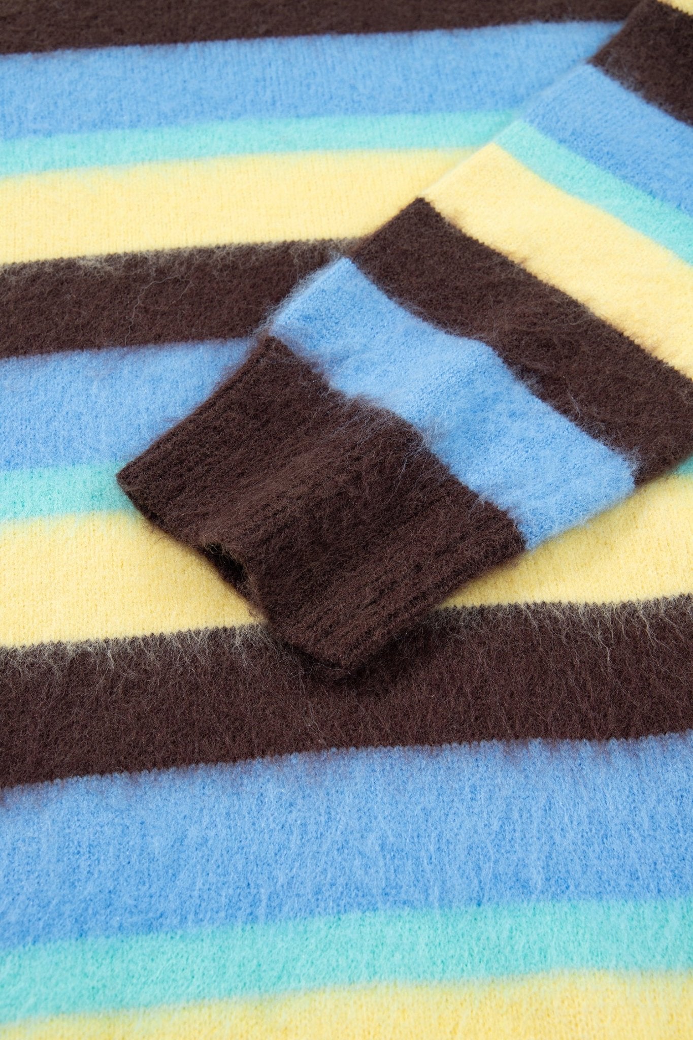 A close-up of a fuzzy striped knit garment, showing alternating horizontal bands 