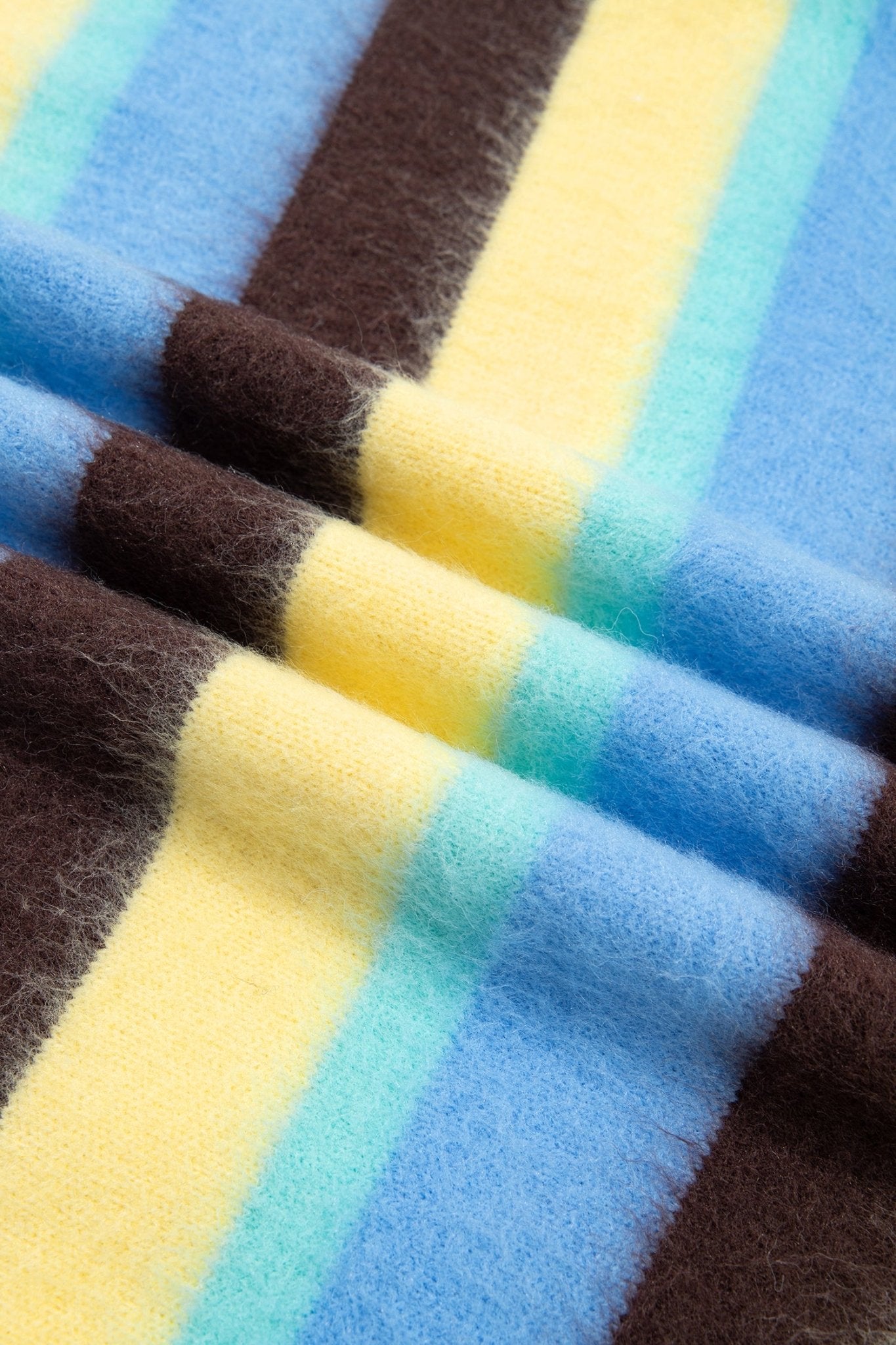 A close-up of a soft, fuzzy striped textile with alternating bands of light blue, yellow, turquoise, and dark brown.