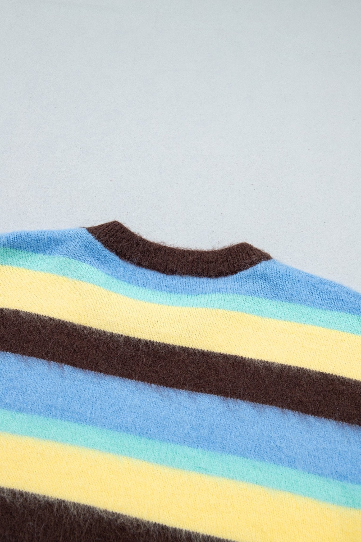 A close-up of a fuzzy striped knit garment showing horizontal bands of dark brown, light blue, pale yellow,