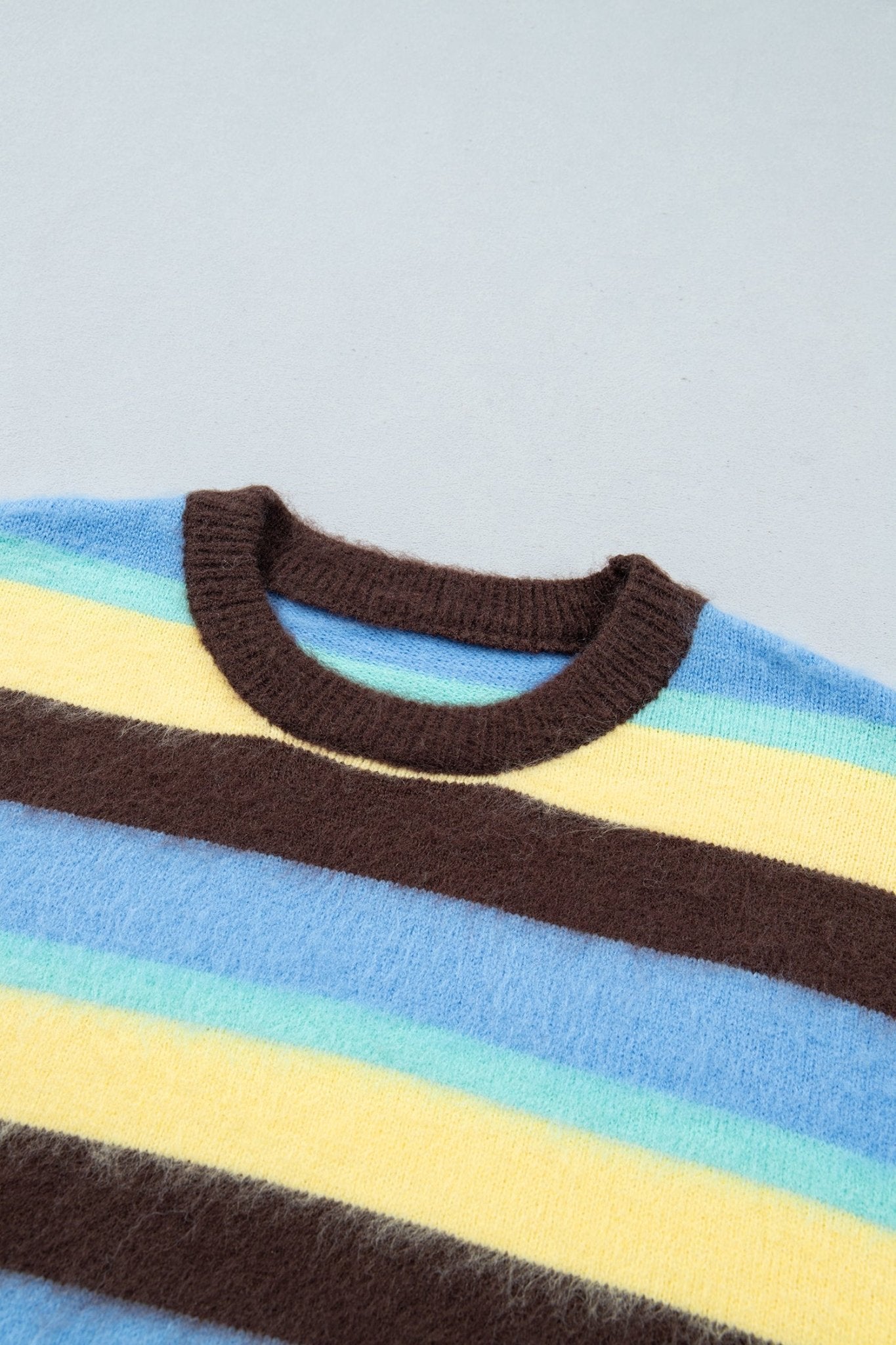 Close-up of a fuzzy striped knit sweater with a dark brown ribbed crew neck, featuring horizontal stripes of light blue