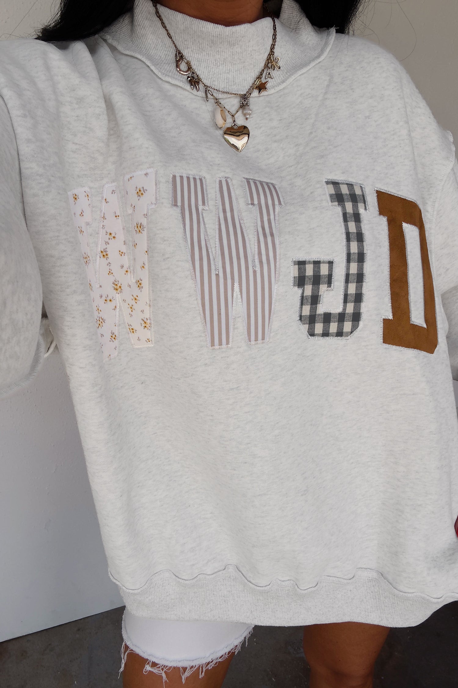 Woman in gray WWJD patchwork letter sweatshirt with white denim shorts