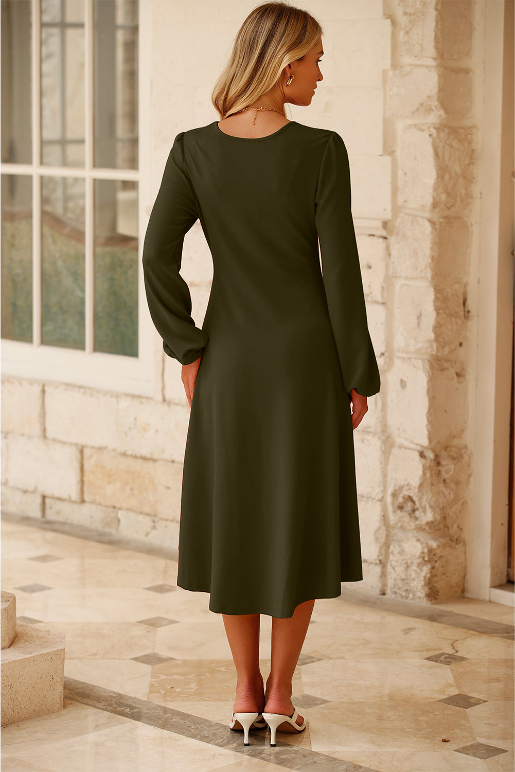 Back view of jungle green midi dress in a sunlit stone corridor