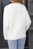 Person wearing a white sweater and light blue jeans standing in front of a dark door.