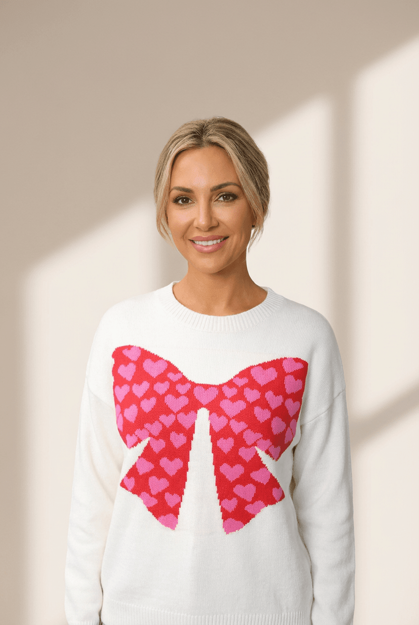 Woman wearing a white sweater with a pink heart bow design on a beige background