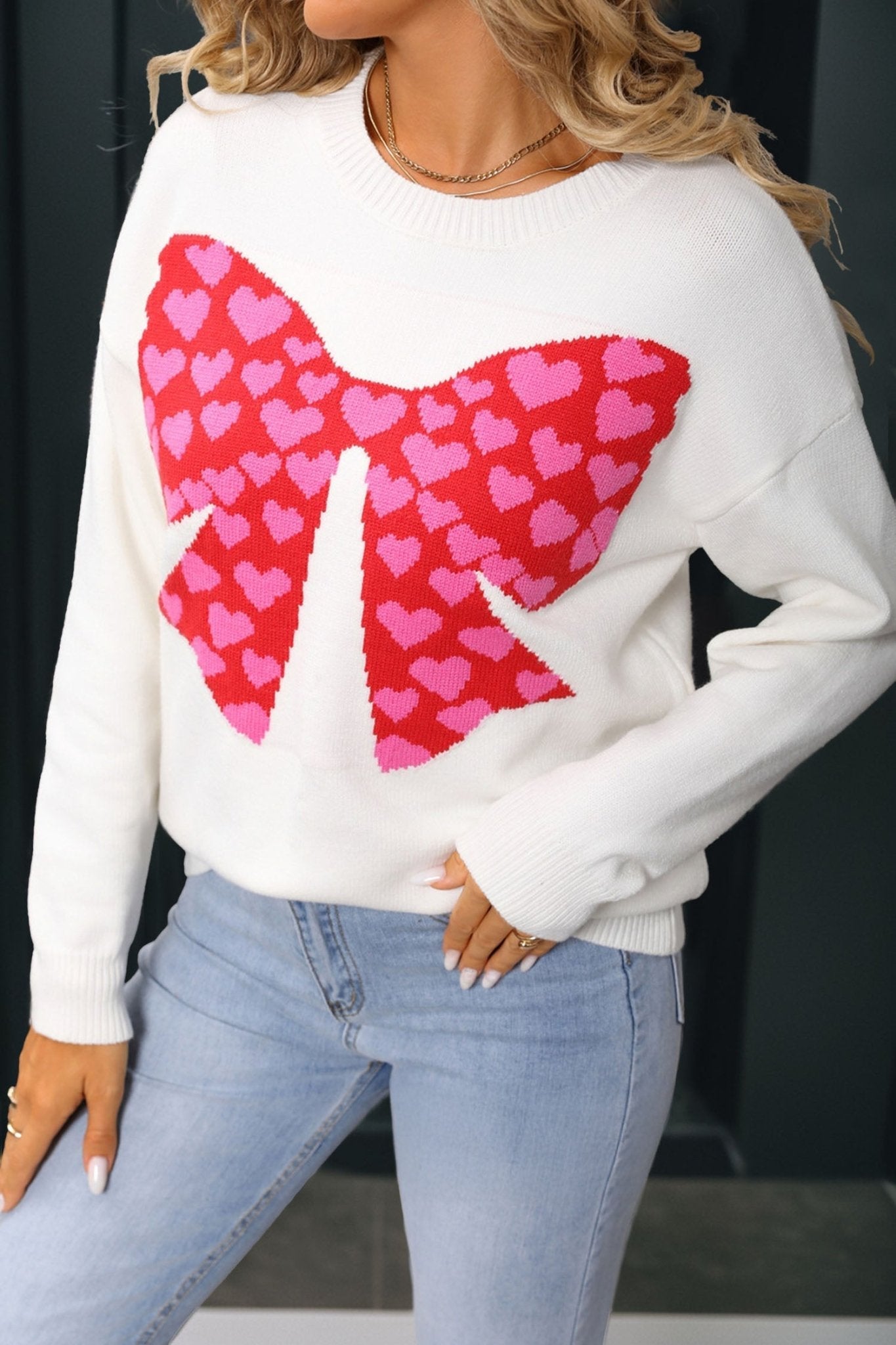 White sweater with a red heart bow design worn by a person.