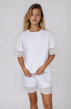 Woman wearing a white outfit with lace details on a plain background