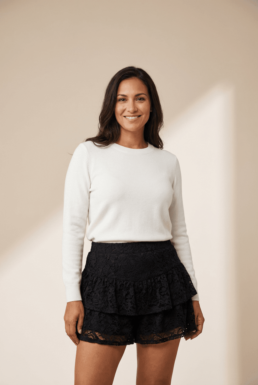 Woman wearing a white sweater and black layered skirt against a beige background