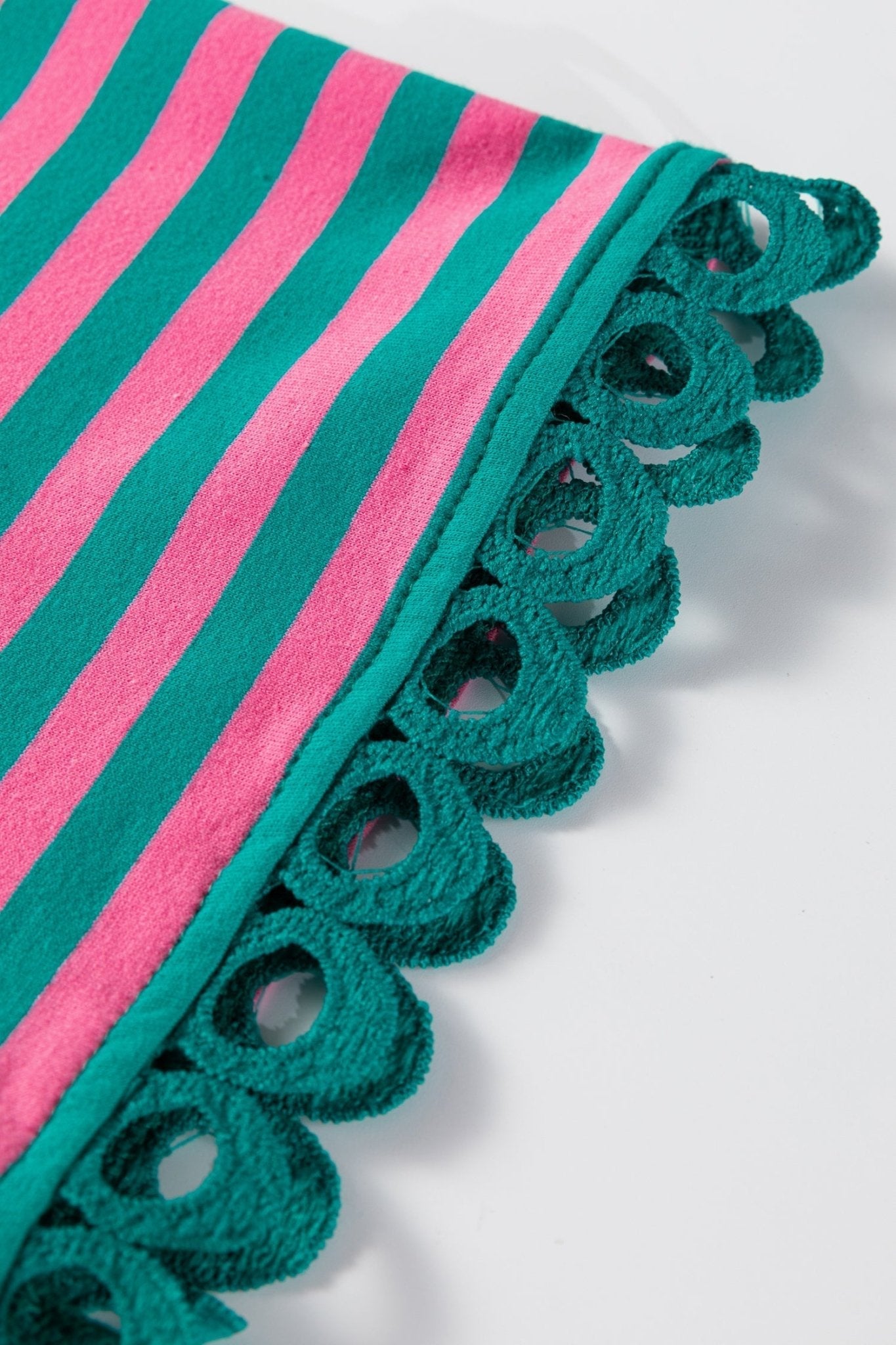 Close-up of a green and pink striped fabric with scalloped edge on a white background