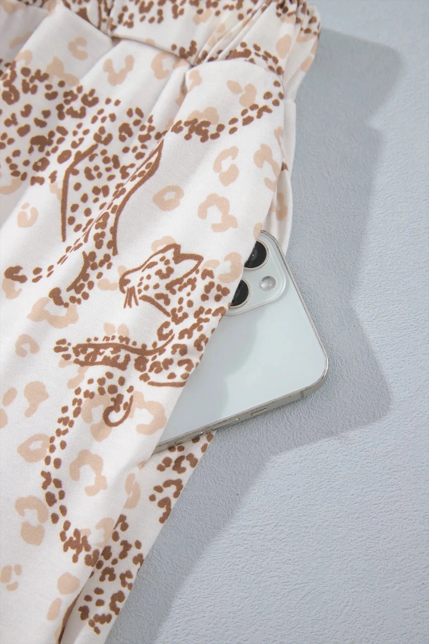 Close-up of beige leopard-print fabric draped over a silver smartphone.