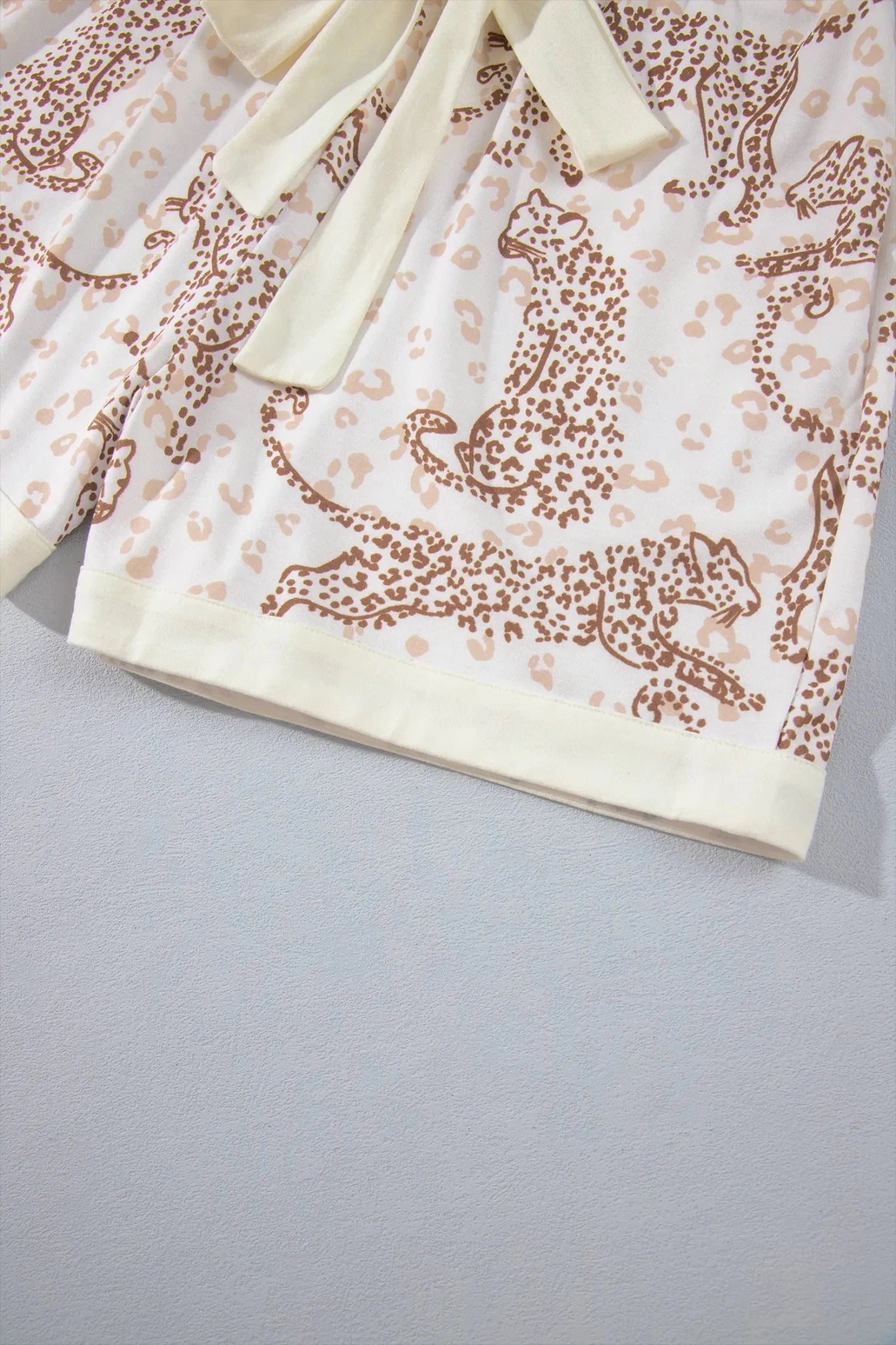 Close-up of cream leopard-print shorts with matching tie belt and solid hem.