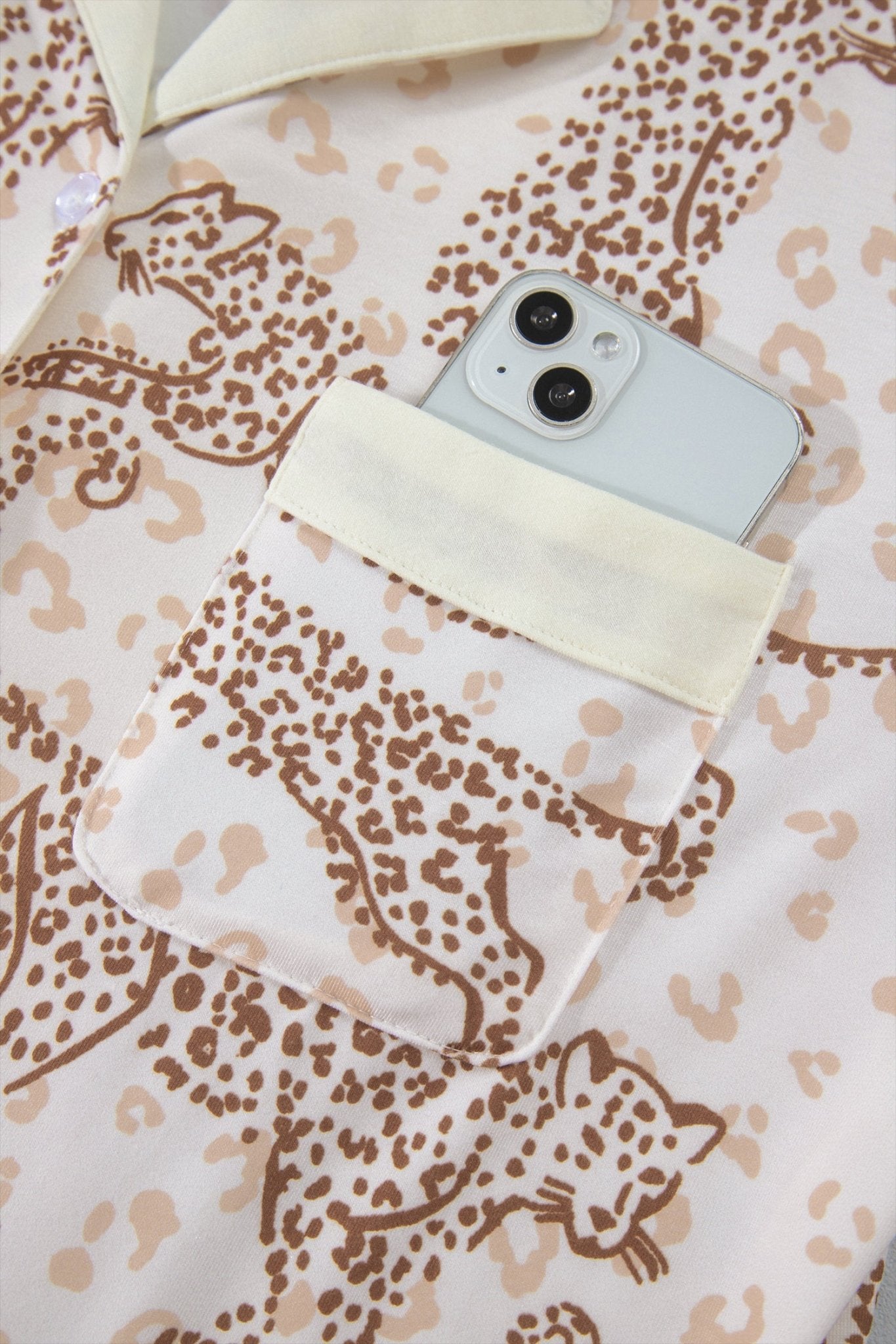 Close-up of cream animal-print shirt with pocket holding a silver smartphone.
