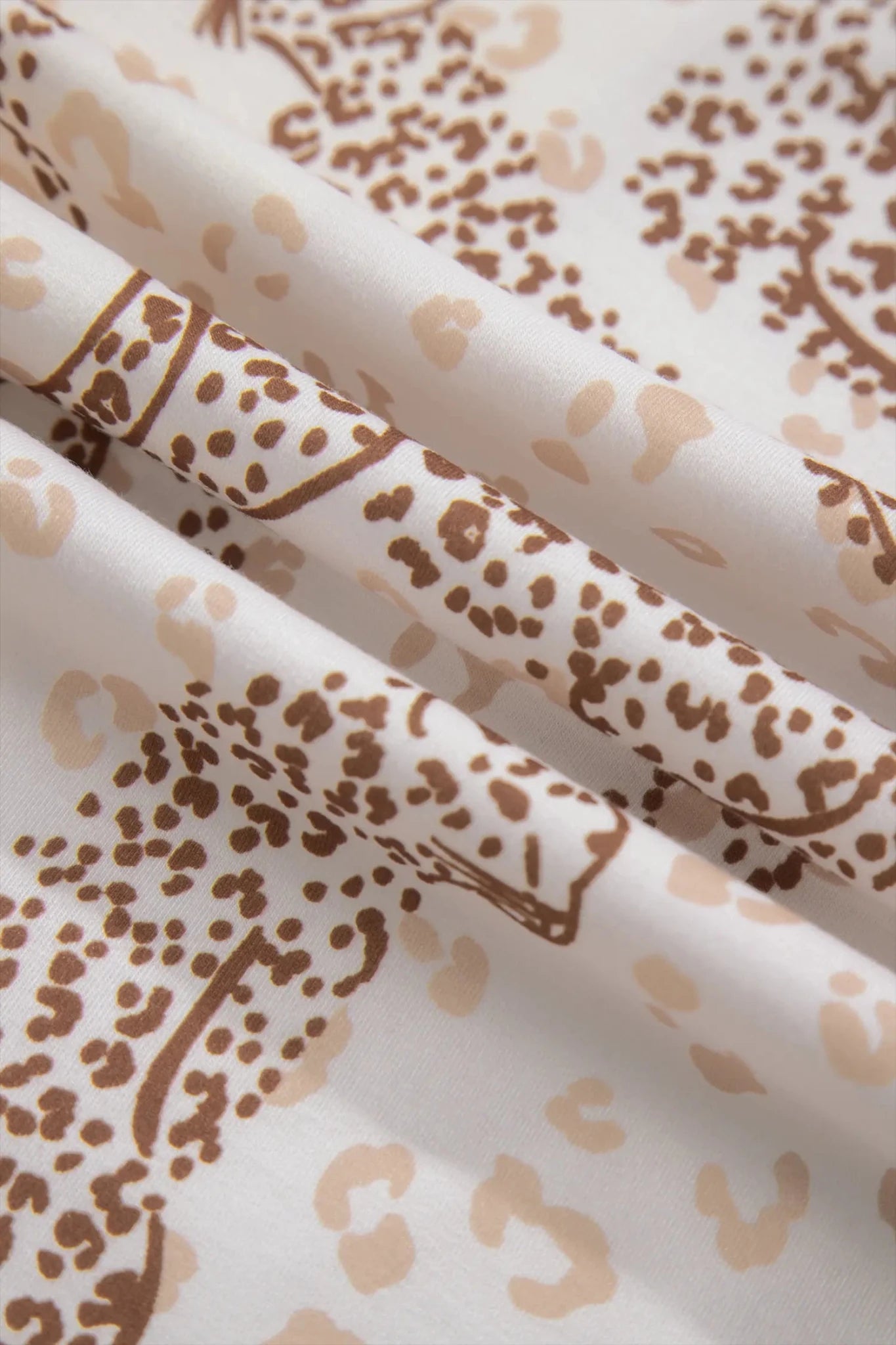 A close-up of draped fabric with an allover leopard print pattern in brown and beige on a white background.