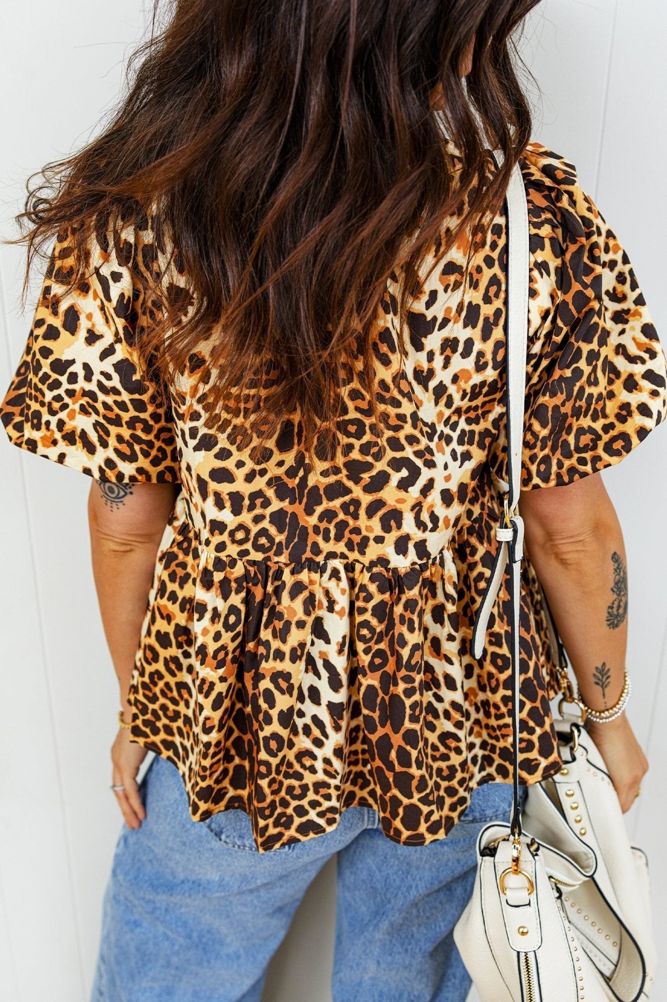 Person wearing a leopard print top and blue jeans, holding a white handbag.