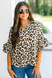 Woman wearing a leopard print blouse with ruffled sleeves outdoors.