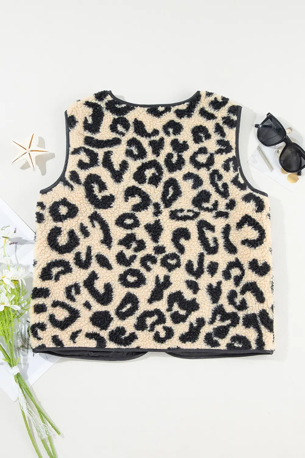 Leopard print sleeveless top on a white background with sunglasses and greenery.