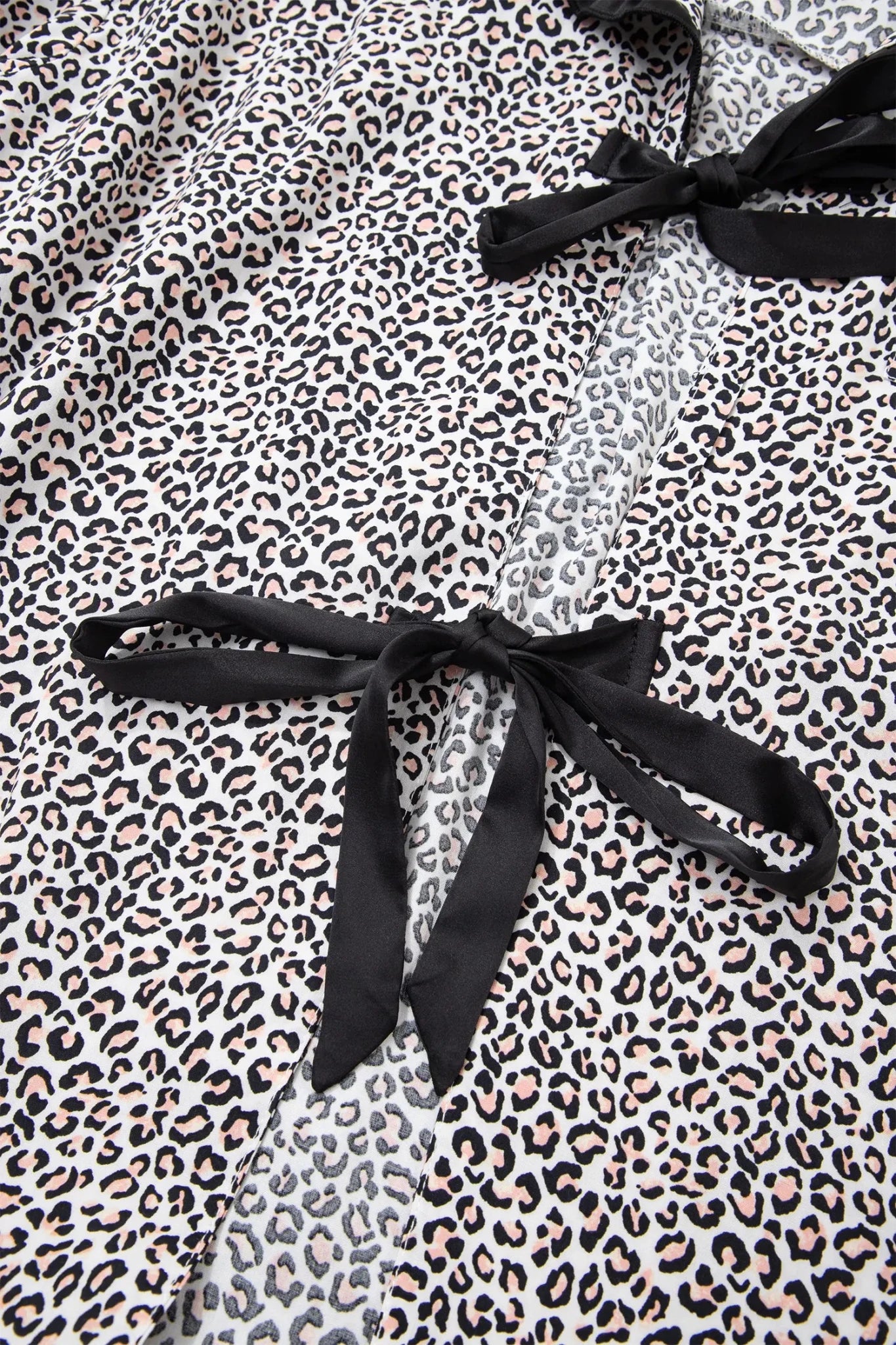 Close-up of a leopard print garment with black satin tie details on a white background.