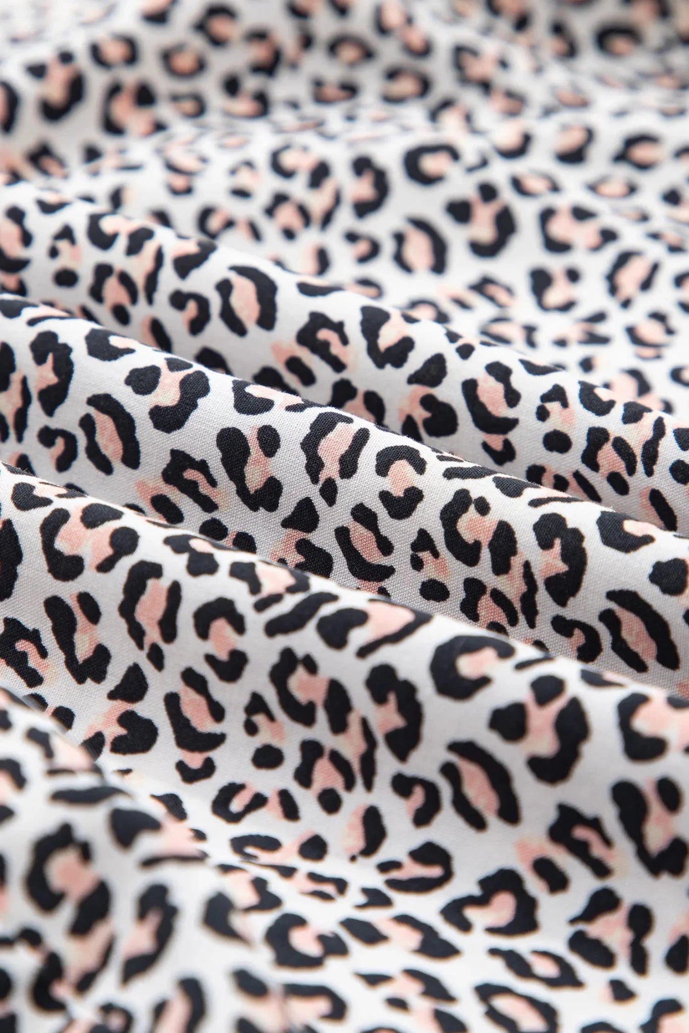 A close-up of draped fabric with an allover leopard print pattern in black, dusty pink, and white.