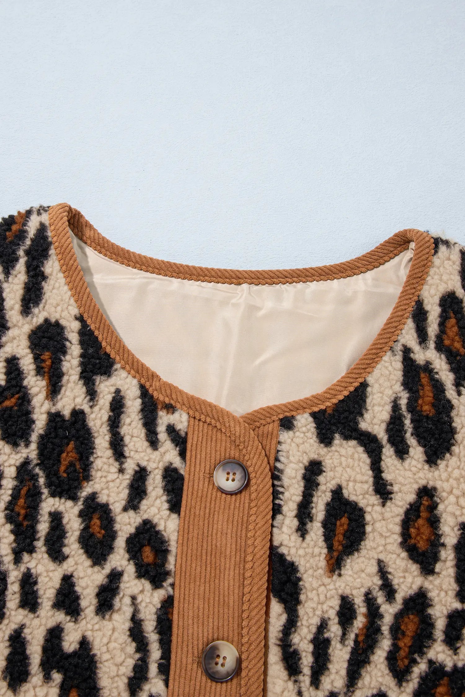 Close-up of corduroy trim and button closure on leopard sherpa jacket