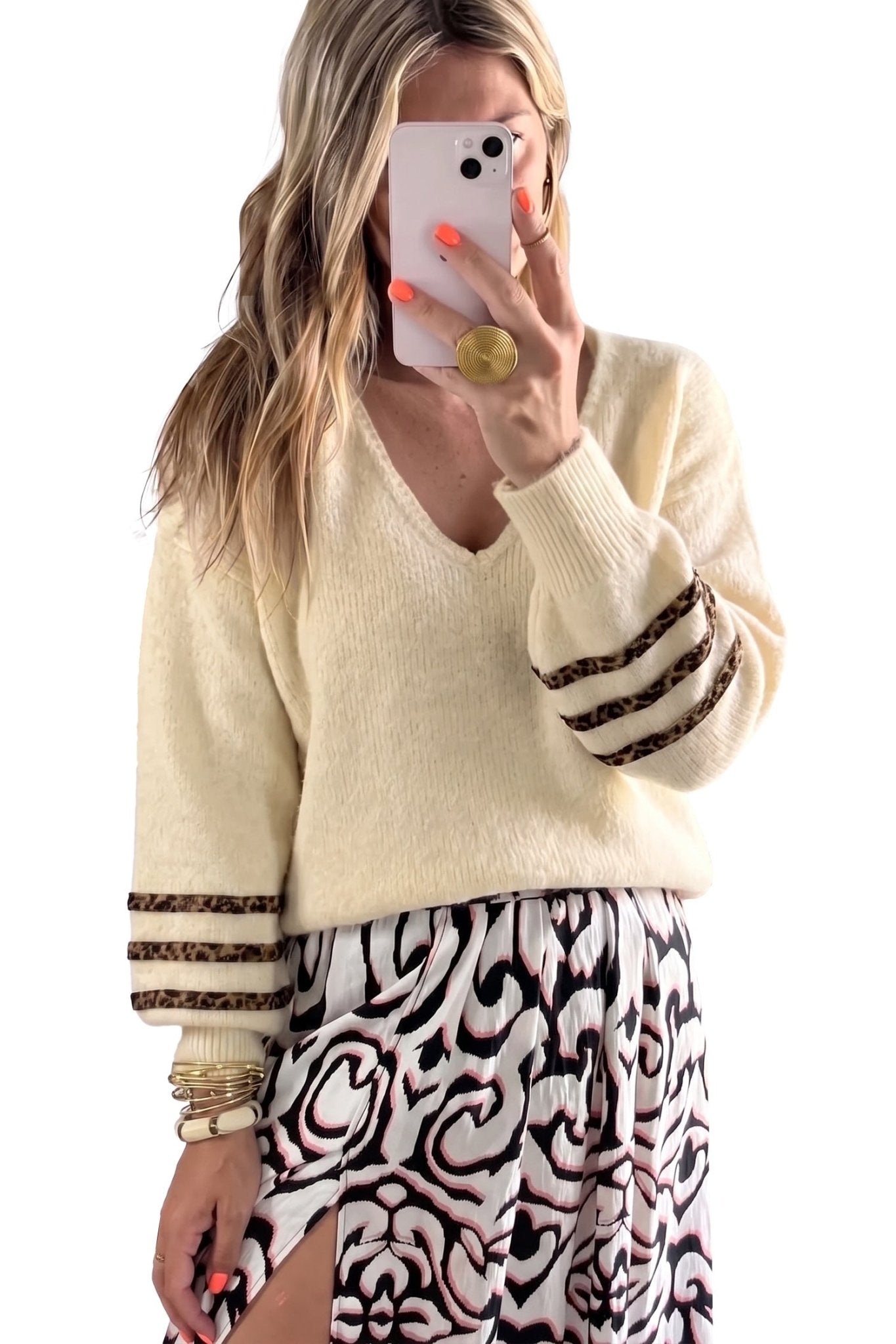 Woman taking a mirror selfie in a cream knit sweater and leopard-print cuffs.