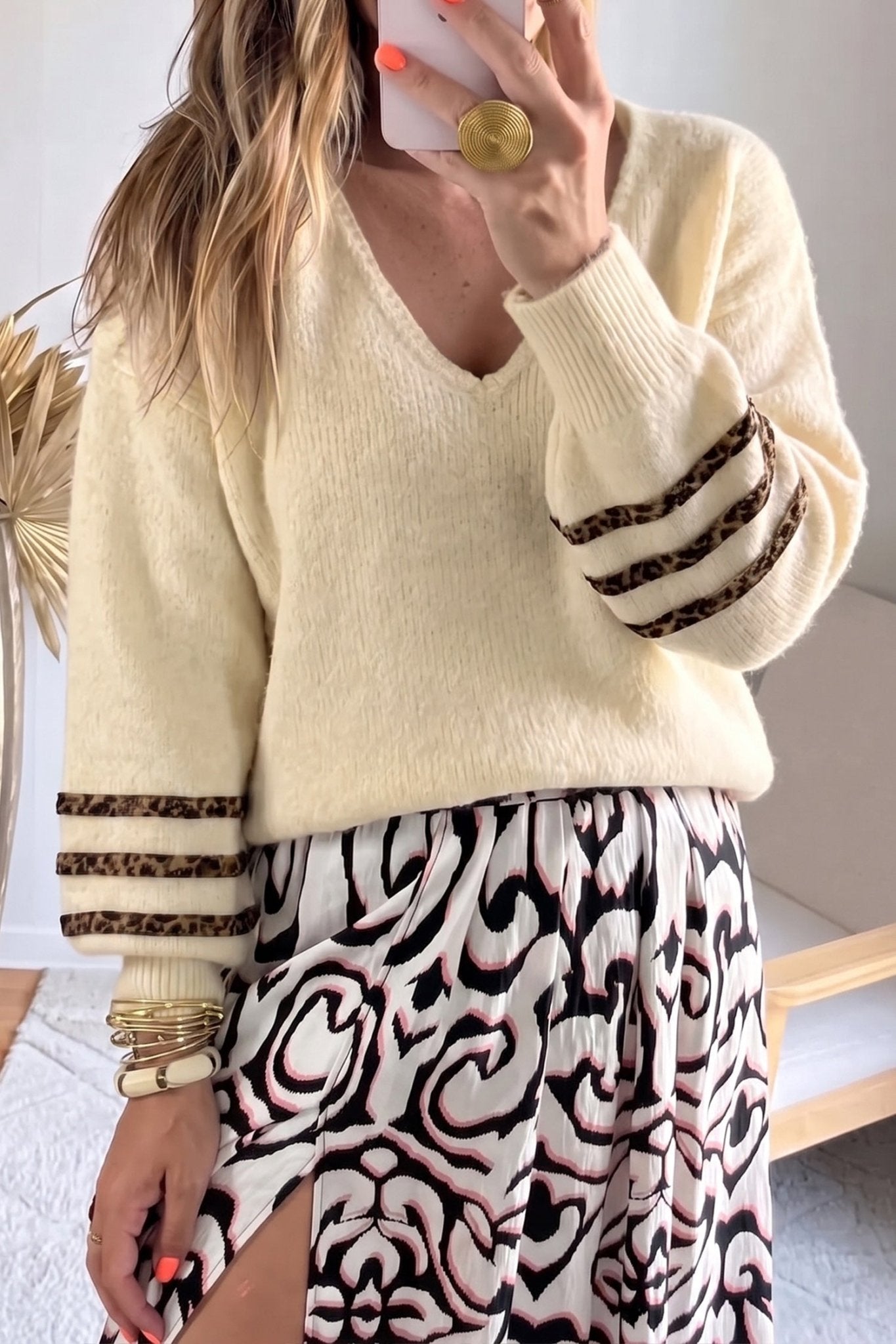 Woman wearing a cream knit sweater with leopard sleeves and a patterned skirt.