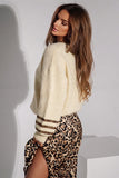 Woman in a cream fuzzy cropped sweater and leopard print skirt with thigh-high slit.