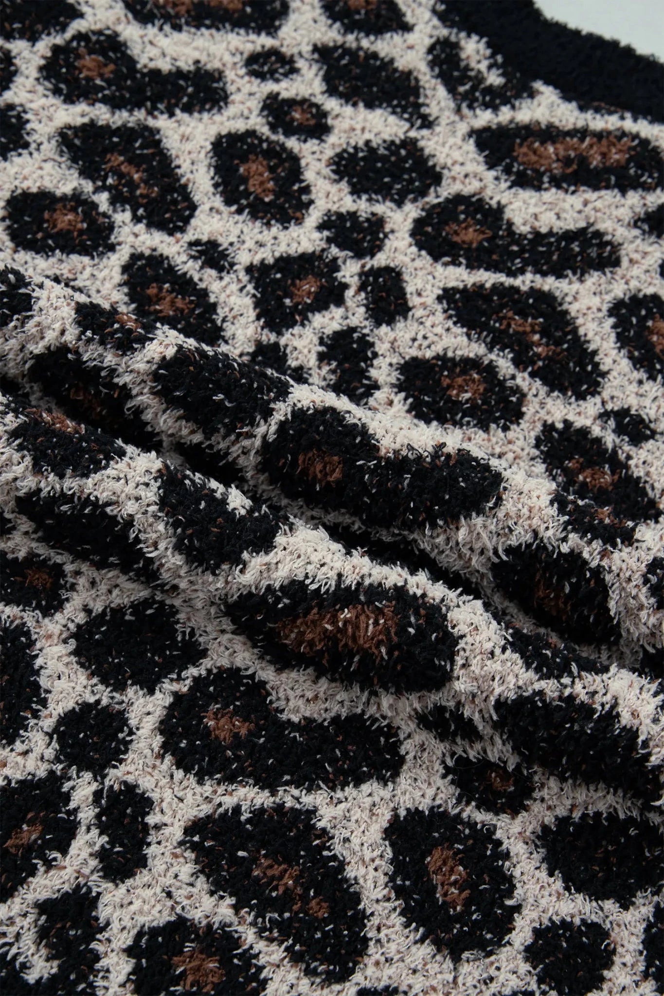Close-up of a plush knit fabric with a leopard print pattern in black, beige, and brown.