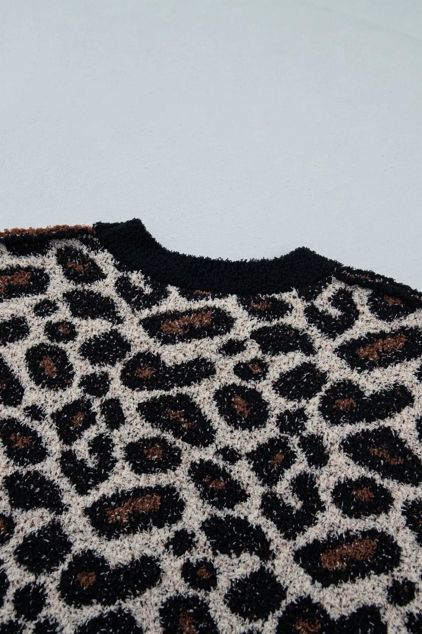 Close-up of knit sweater with black-brown-cream leopard print and black ribbed crew