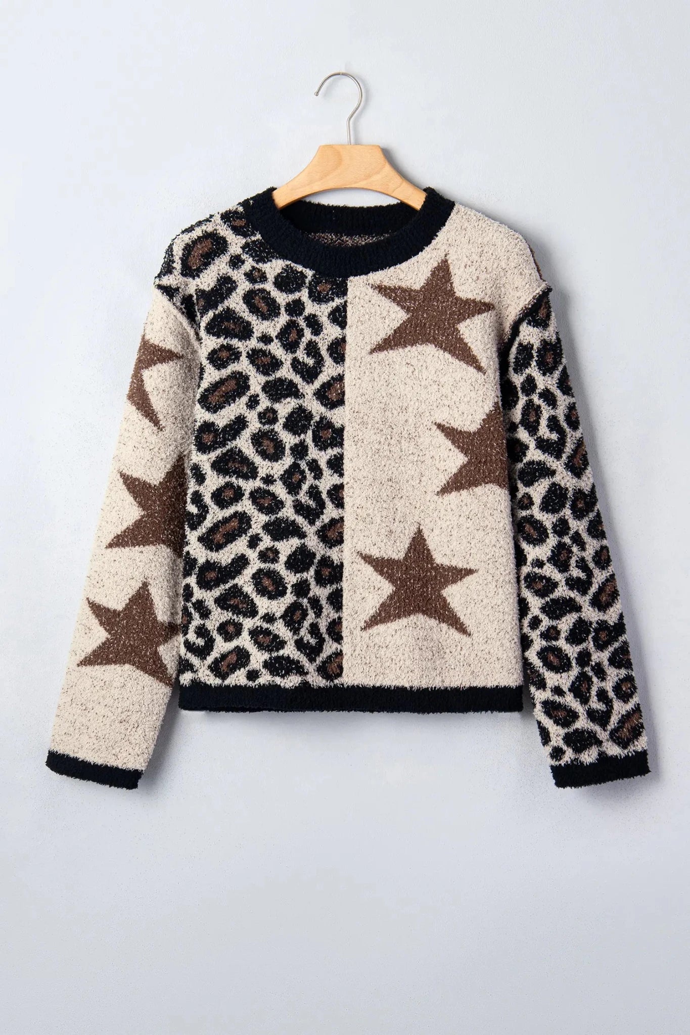 A fuzzy knit sweater with a leopard print and star pattern, hanging on a wooden hanger against a light gray background.