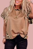 Woman wearing a beige top with leopard print sleeves against a pink background