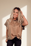 Woman wearing a beige top with leopard print sleeves against a neutral background