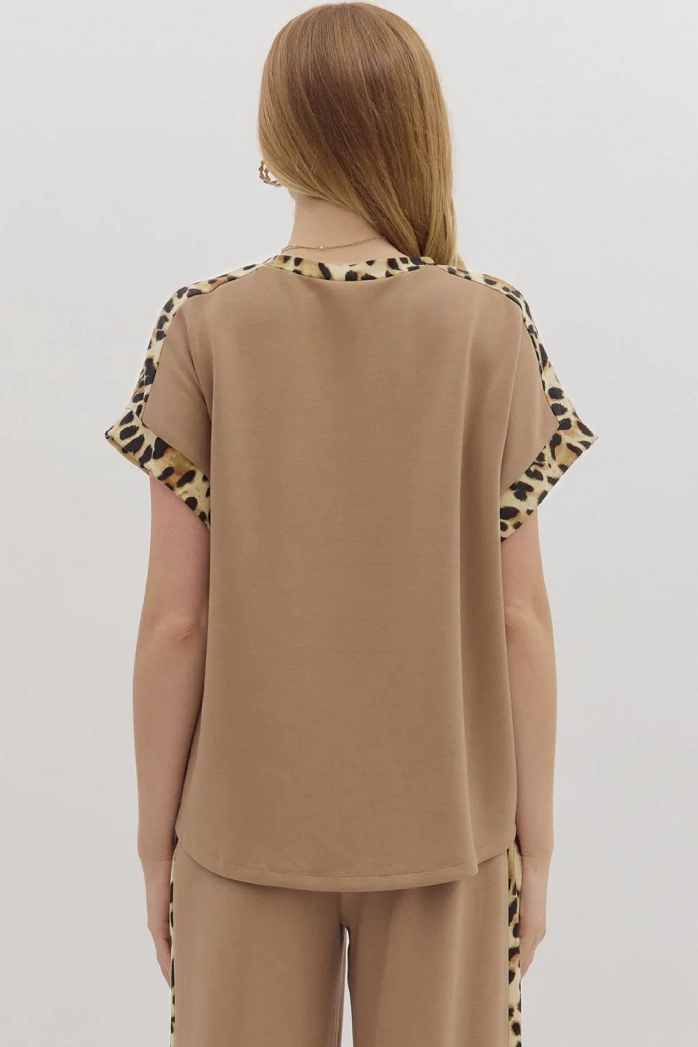 Person wearing a beige top with leopard print sleeves on a plain background