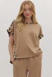 Woman wearing a beige outfit with leopard print sleeves on a plain background