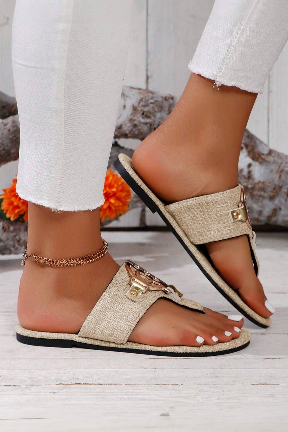 Beige sandals with gold accents worn by a person on a light wooden floor.