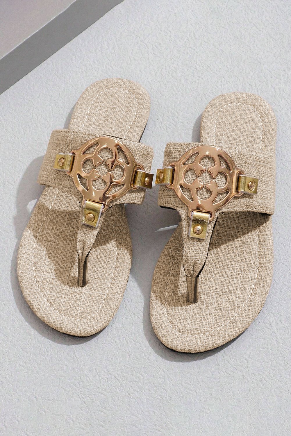 Pair of beige sandals with gold embellishments on a light gray background