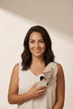 Woman holding a shoe with a decorative brooch against a plain background