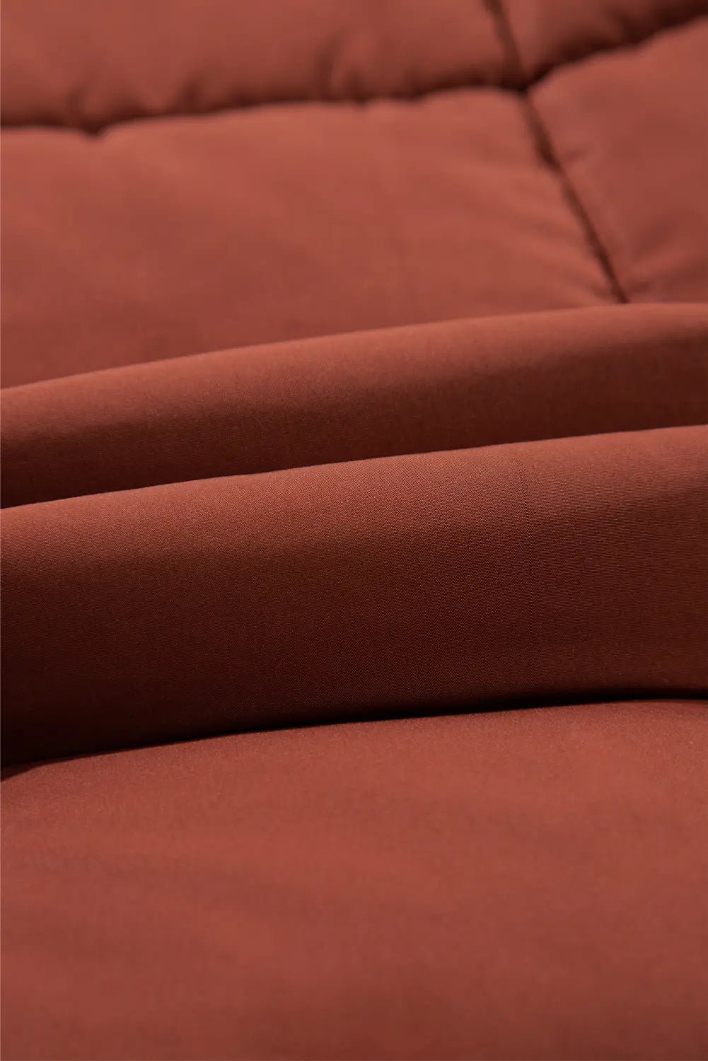 Close-up of a rust-colored, quilted fabric surface with soft folds and stitched paneling.
