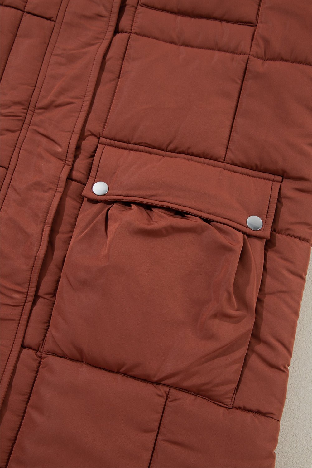 Close-up of a brown quilted jacket with a pocket and button details.
