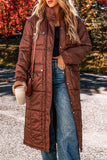Person wearing a long brown quilted coat outdoors with autumn foliage in the background
