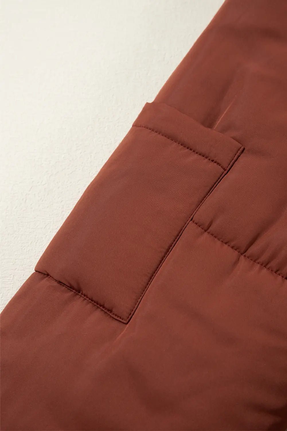 Close-up of a brown puffer jacket with a pocket on a light beige background
