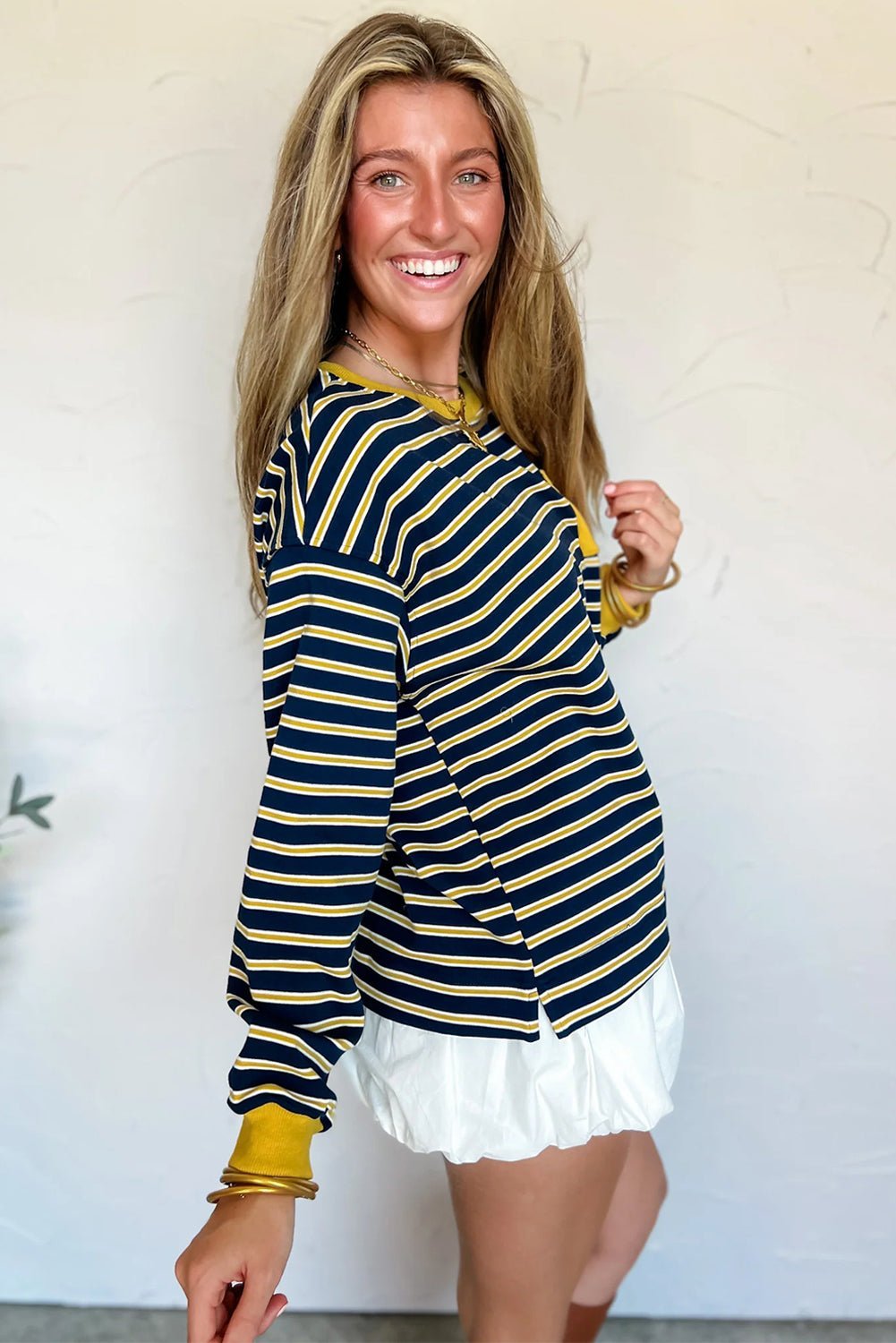 Woman wearing a navy and gold striped long-sleeve top with white shorts against a plain background