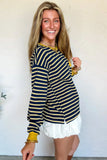 Woman wearing a navy and gold striped long-sleeve top with white shorts against a plain background