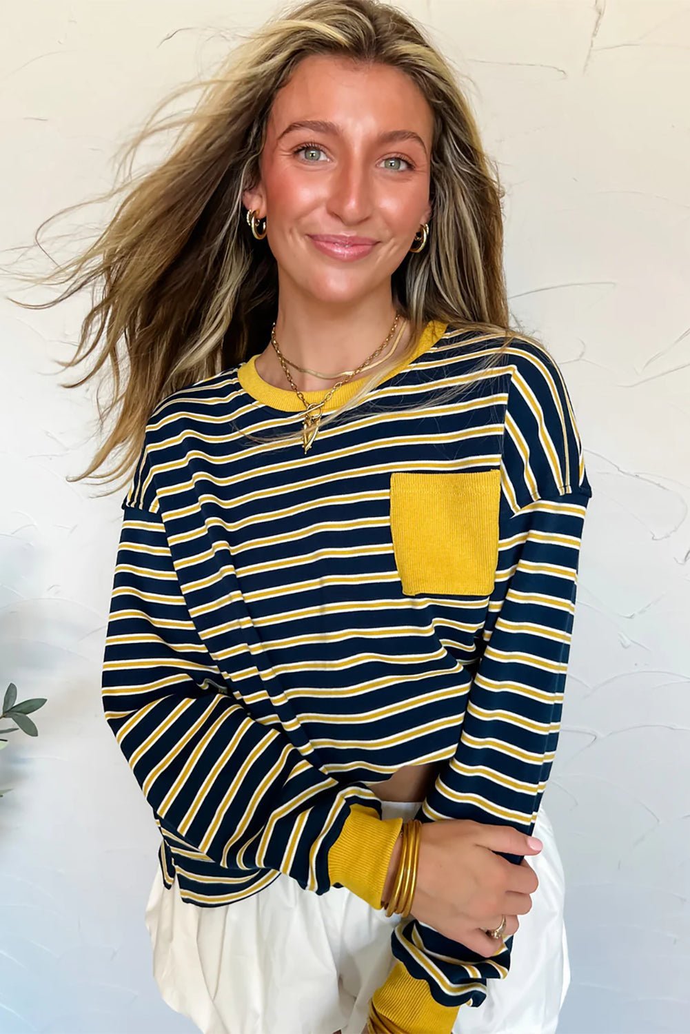 Woman wearing a navy and yellow striped long-sleeve top with a yellow pocket against a light background