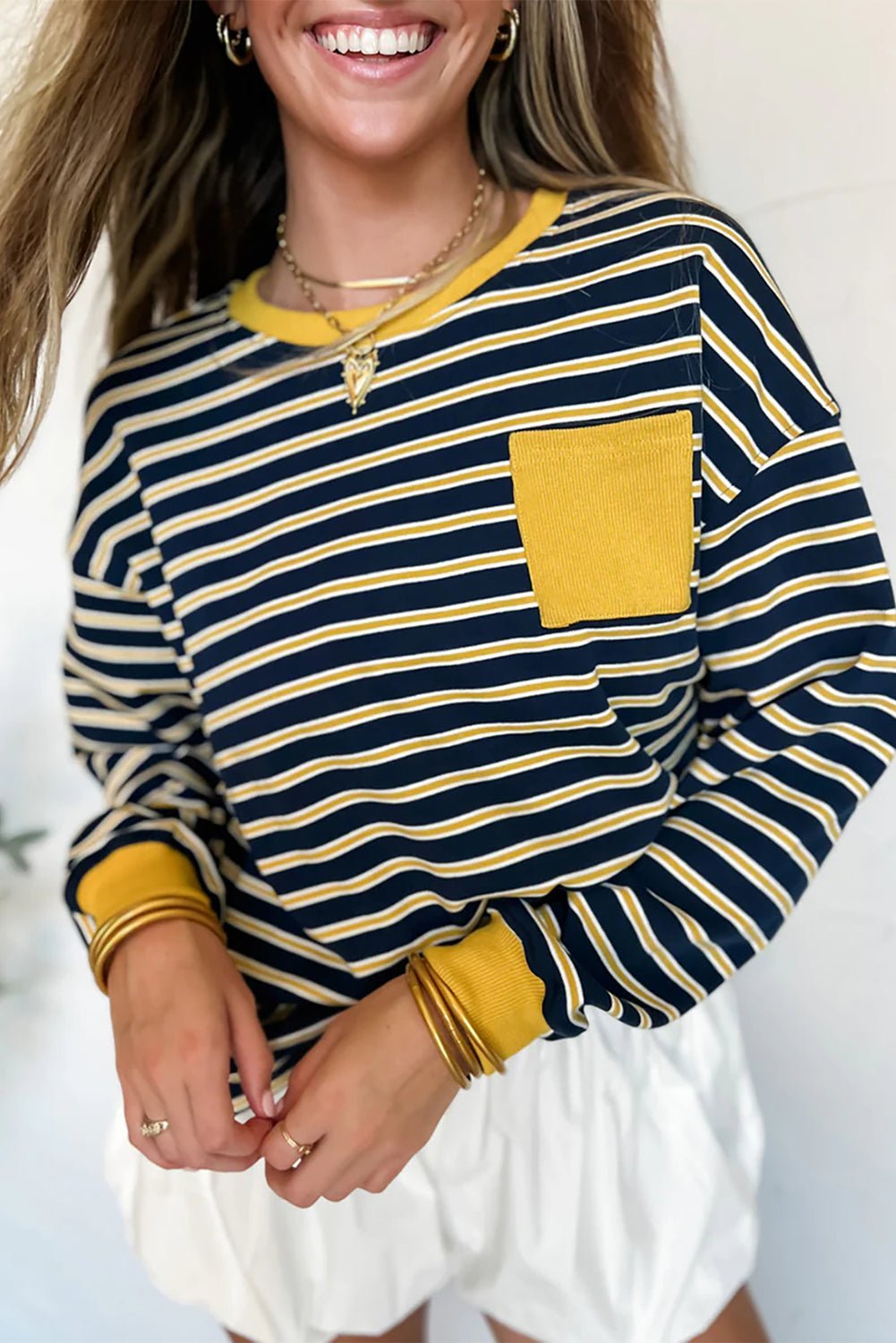 Woman wearing a navy and yellow striped long-sleeve shirt with a pocket on a light background