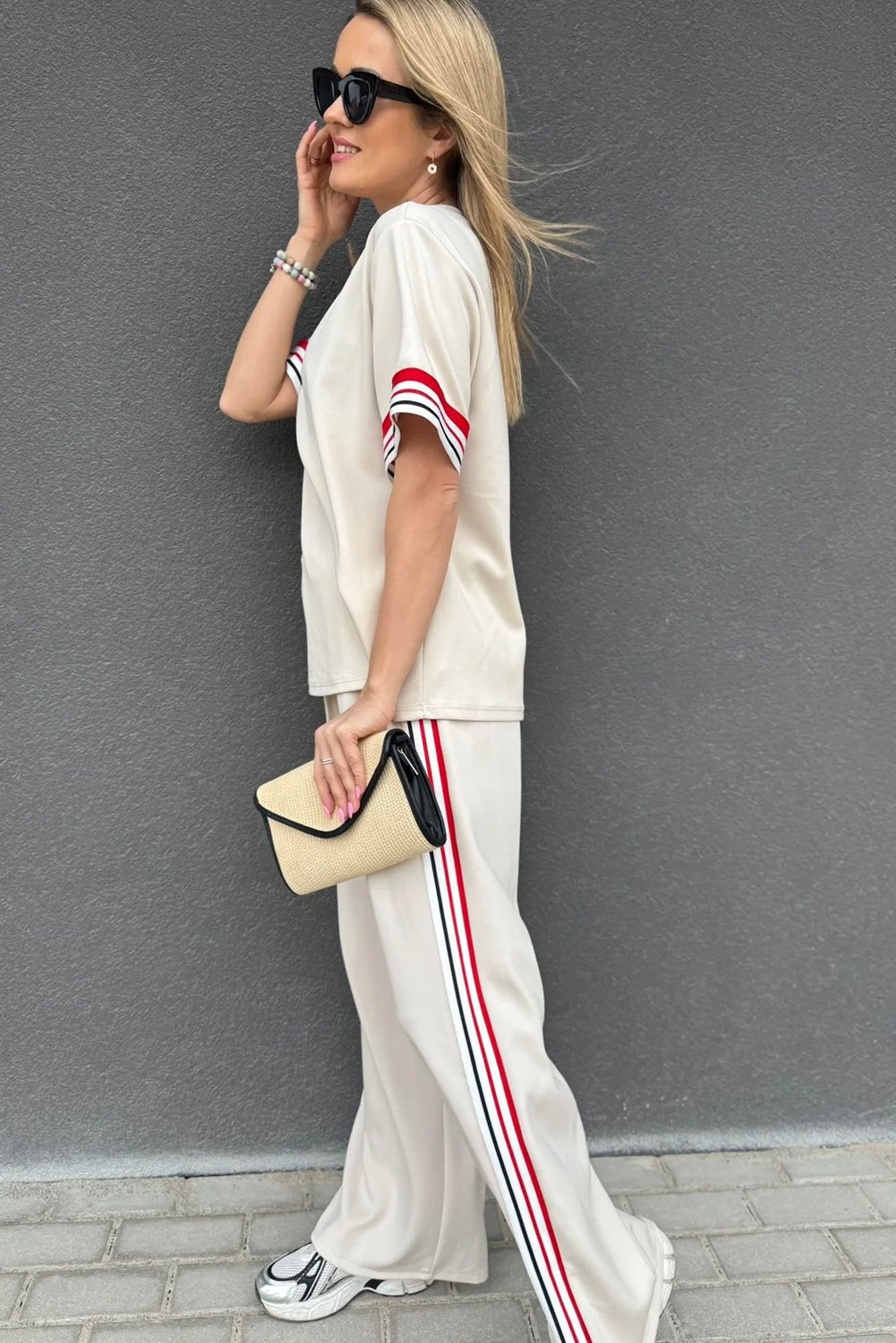 Woman in a casual outfit with a white t-shirt and striped pants against a gray wall.