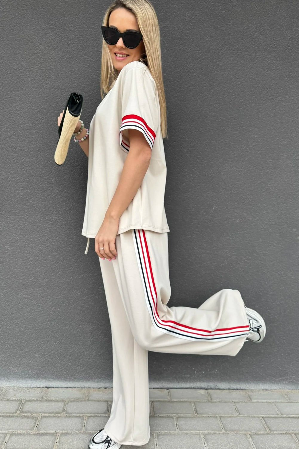 Woman wearing a white outfit with red and blue stripes against a gray wall.
